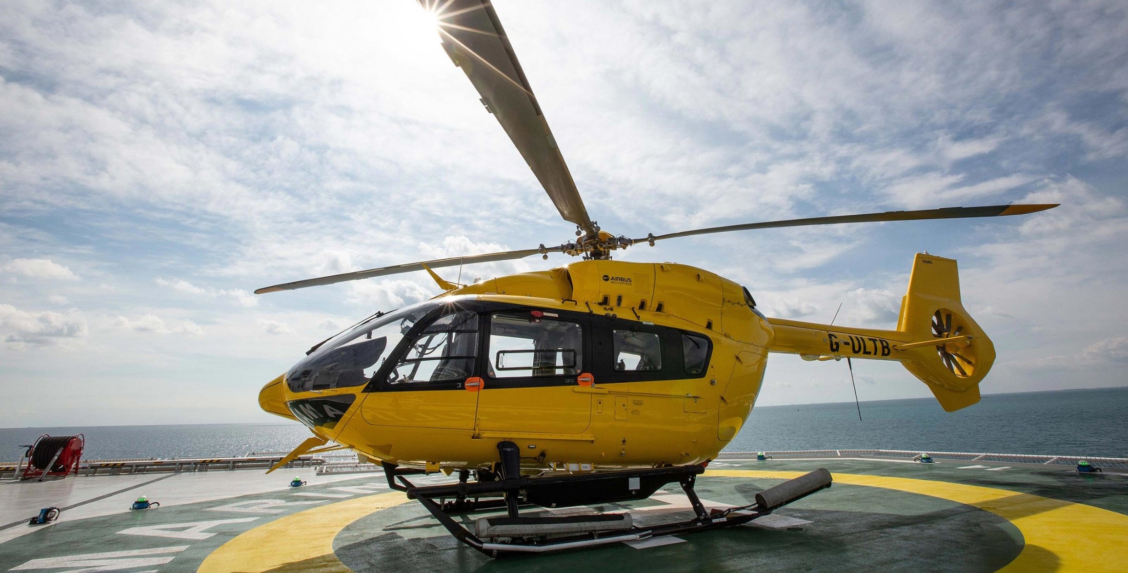 One of Ultramarine's two yellow Airbus H145 helicopters on the ship's helideck, open sea behind.